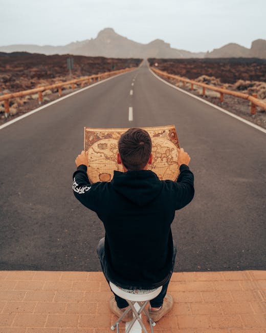 A man sits on a stool holding a map on an open road in Tenerife, Spain, conveying exploration.